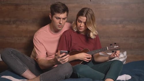 Couple Playing Ukulele and Using Phone on Bed