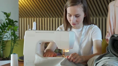 Young Woman Sews Fabric with Sewing Machine