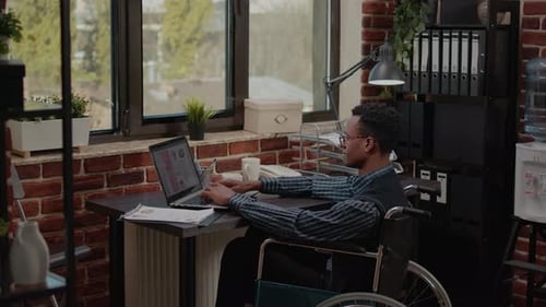 Young Adult in Wheelchair Using Laptop in Office