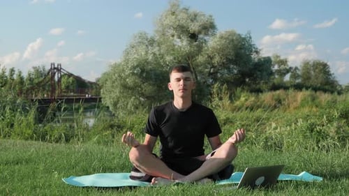 Man Meditating Outdoors on Grass Near Water