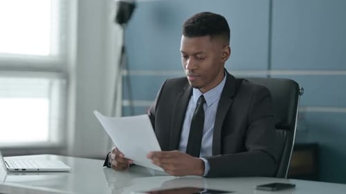 African Businessman Celebrating Success while Reading Documents in Office