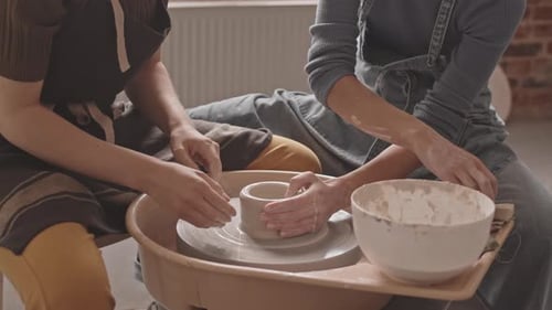 Women molding clay pot on pottery wheel