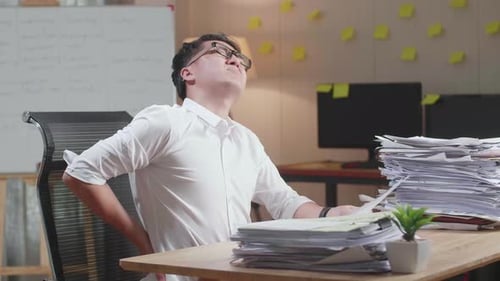 Asian Man Having Backache While Working Hard With Documents At The Office