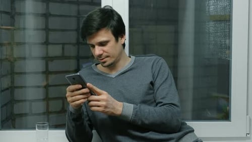 Adult Using Smartphone While Leaning Against Window