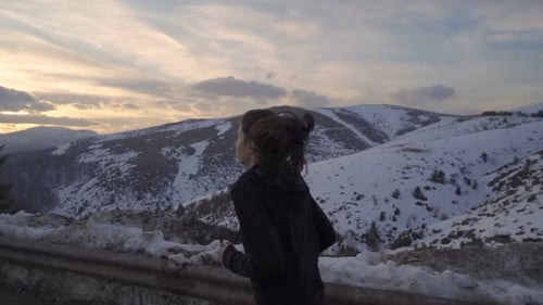 Woman Runs Along Snowy Mountain Road at Sunrise