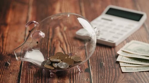A Hand Inserting Coins in Piggybank Over Wooden Desk