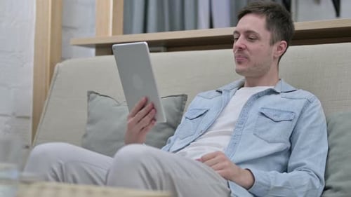 Man Using Tablet for Video Call on Couch