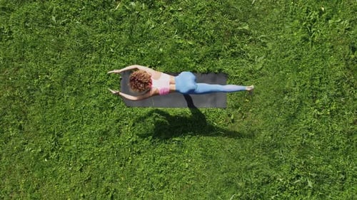 Top View of flexible slender woman doing yoga on the green grassy lawn.