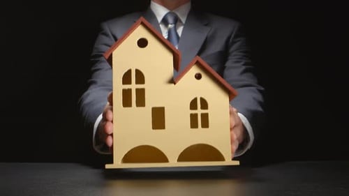 Businessman Presents Model House on Black Background