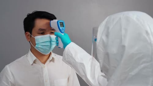Arzt im PPE-Schutzanzug verwendet ein Infrarotthermometer, um die Temperatur mit Personen zu messen