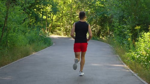 Man Jogging on Road Among Trees in Slow Motion