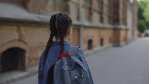 Rückansicht eines kleinen Mädchens, das in Jeansjacke in der Nähe der Schule auf der Straße herumläuft
