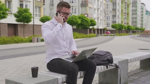 Man Using Laptop and Phone Outdoors in City