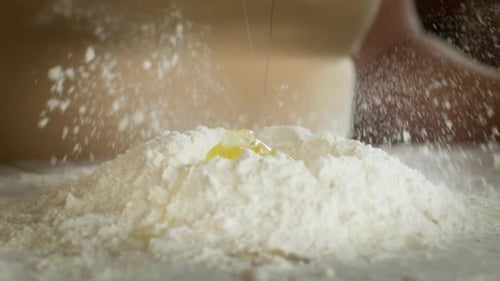 Close Up Cracking Raw Egg Over Flour on Table Powdering with Flour, Baking