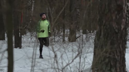Young Man Athlete Running Through Winter Forest