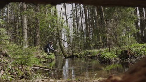 Mann sitzt allein am Flussufer zieht Ast mit Zweig heraus reinigt Teich