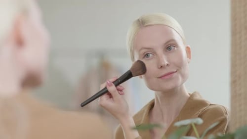 Woman Applying Makeup with Brush in Front of Mirror