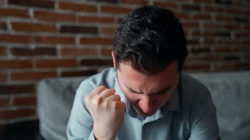 Stressed Young Man with Headache Sits on Couch