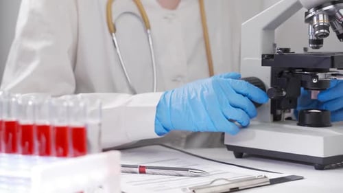 Medical Professional Working with Microscope and Blood Samples