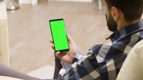 Young Man on the Couch Looking at Green Screen Phone