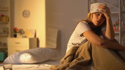Sick Lady With Towel on Forehead Suffering From Migraine, Lying in Bed at Home
