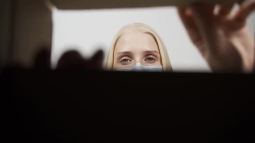 Blonde Woman Wearing Mask Peeks Into Open Box