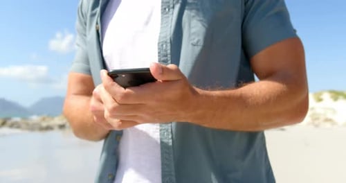 Mid section of man using mobile phone at beach on a sunny day 4k