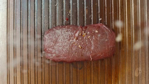 Spices and Salt are Poured on a Piece of Beef Lying on the Grill