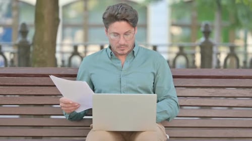 Man Works on Laptop While Sitting on Park Bench