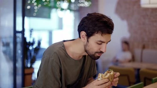 Young Adult Man Enjoys Sandwich at Cafe