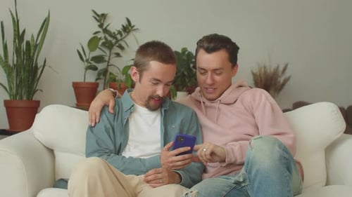 Lgbt Men are Sitting on the Sofa in the Living Room and Watching Something on the Phone in the