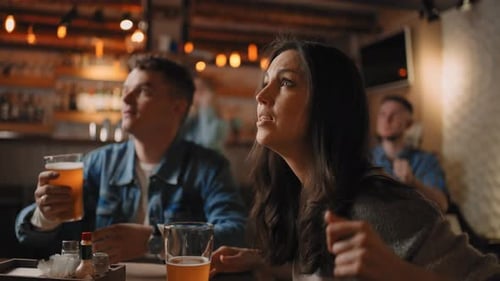 Closeup of a Group of Male and Female Friends Sitting Together in a Bar and Watching a Broadcast on
