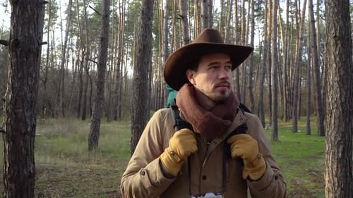Backpacker with Camera Walks Along a Trail in the Forest