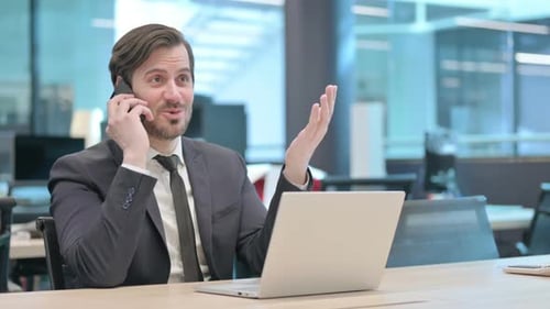Businessman Talking on Phone While Using Laptop in Office