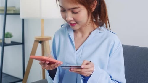 Young Asia lady use smart phone, credit card buy and purchase e-commerce internet at home.