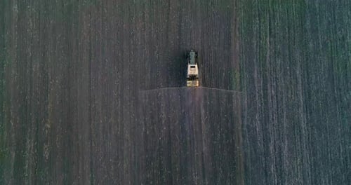 Tractor with trailed sprayer spraying chemicals on agricultural field. Aerial view.