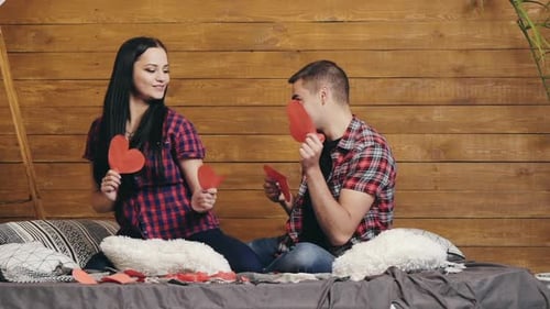 Smiling Couple Tossing Red Hearts on Bed
