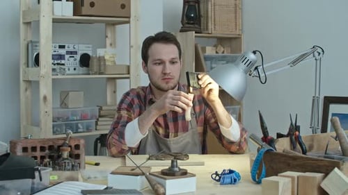 Young Adult Male Crafts Object at Workshop Desk