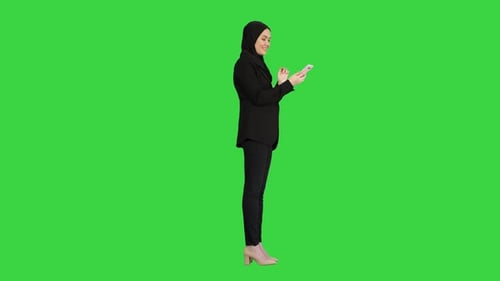 Muslim Girl in Hijab Using Smartphone To Send Voice Messages on a Green Screen, Chroma Key.