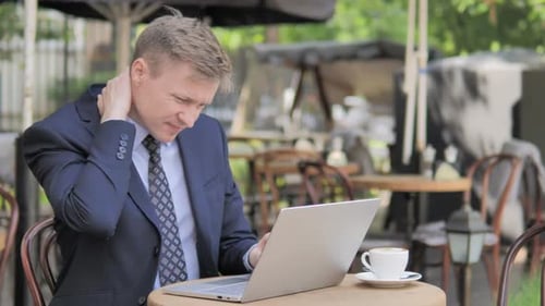 Man Working on Laptop, Rubbing Neck Outdoors