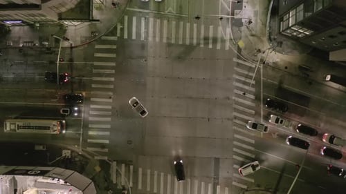 VUE AÉRIENNE : Le ciel s'élève de nuit sur une rue à l'intersection avec des rues lumineuses et une circulation de voitures de ville