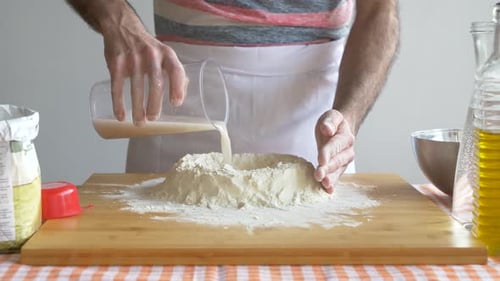 Mann gießt Wasser in Mehl für die Zubereitung von Pizzateig