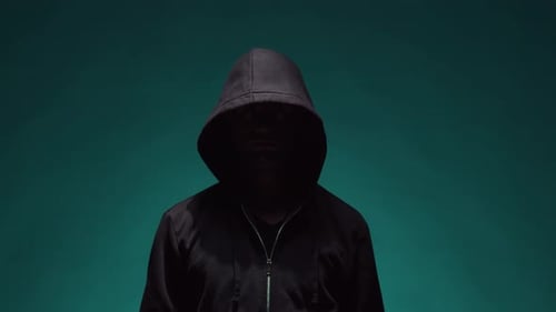 Enigmatic Hooded Figure Raising Hand Against Teal Backdrop