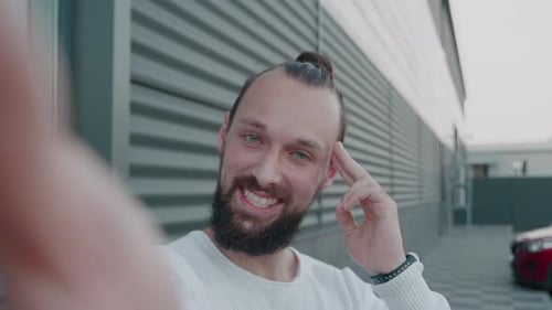 Aufnahme eines jungen bärtigen Mannes, der Online-Videoanrufe tätigt und spricht und dabei die Kamera im Freien betrachtet und
