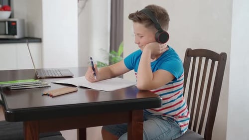 Boy Studying and Writing with Headphones on at Home