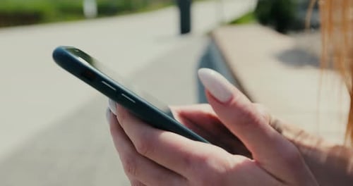 Closeup of Woman Hands with Smartphone Texting Messenger on the Street Bench