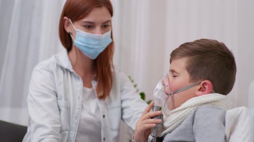 Young Boy Uses Nebulizer with Mother Nearby