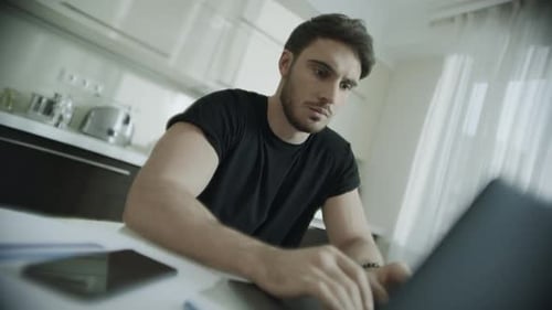 Ernsthafter Mann tippt Laptop zu Hause. Geschäftsmann benutzt Computer in der Küche