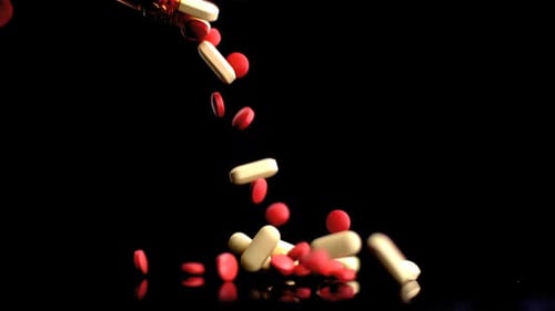 Red and White Pills Falling on Black Surface