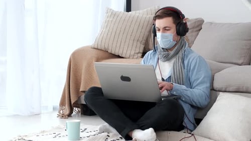 Young Adult with Mask Works on Laptop at Home
